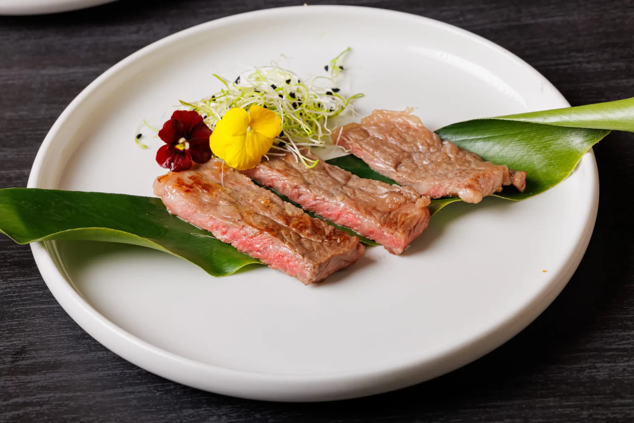 Wagyu fatiado sobre folha verde com flores comestíveis