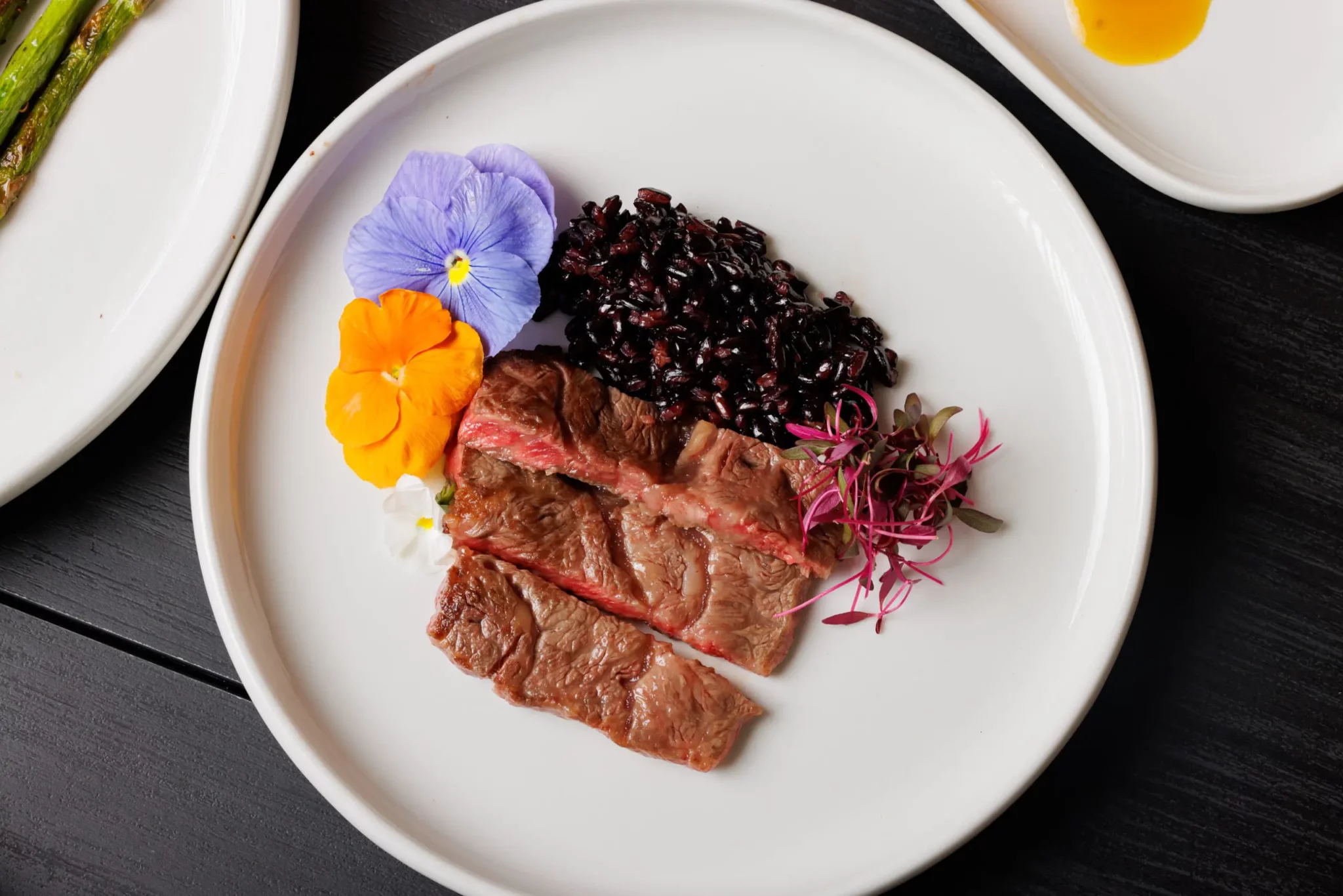 Risotto de arroz negro com corte de carne selecionado e flores comestíveis