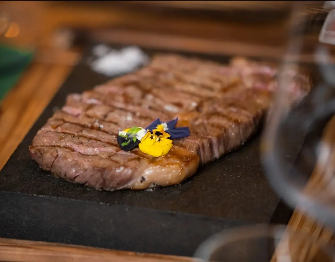 Carne grelhada sobre pedra quente com flores comestíveis